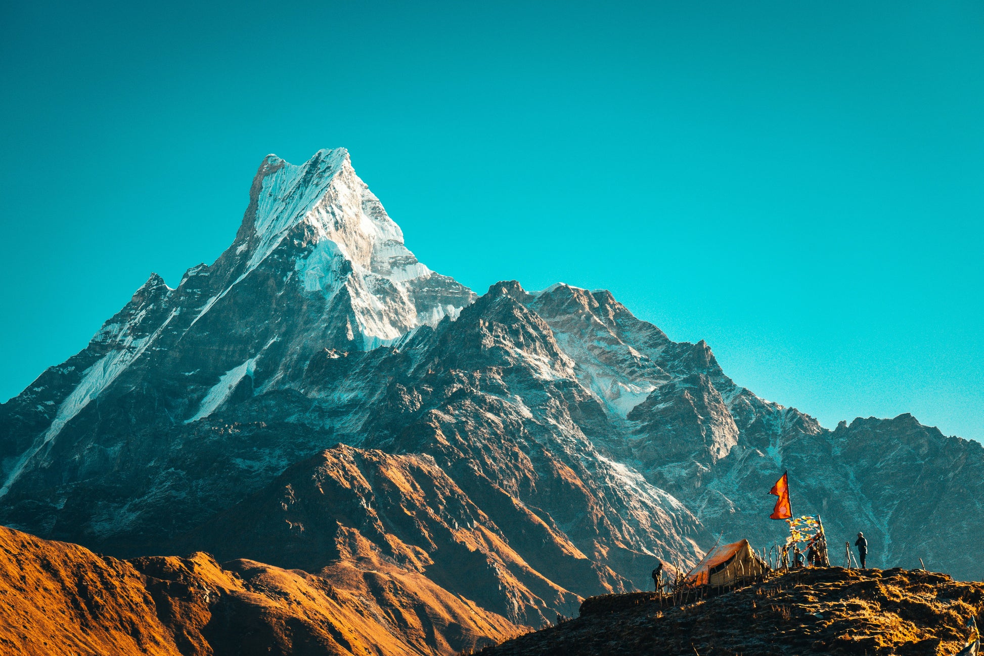 Stretched Canvas: person in orange jacket standing on brown rock near snow covered mountain during daytime – Raimond Klavins (Unsplash)