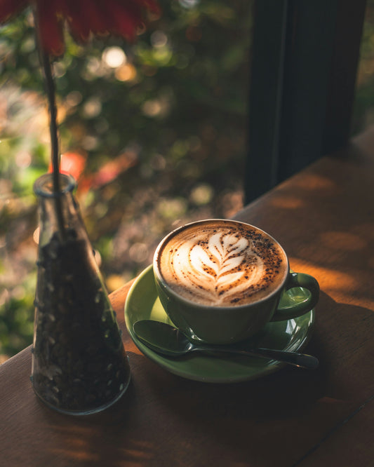 Poster: a cappuccino on a saucer next to a vase with a flower – Kristian Tandjung (Unsplash)